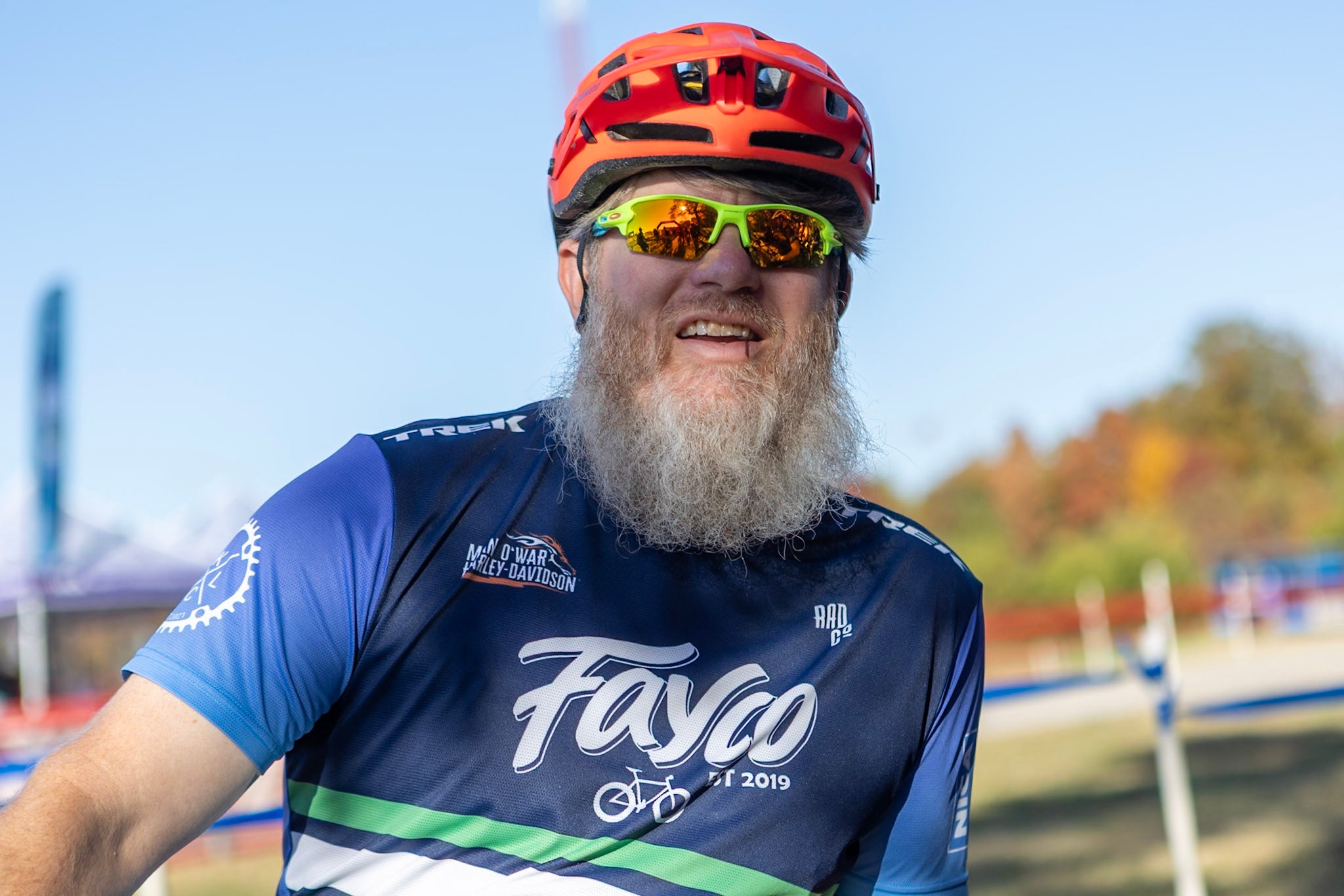 Man wearing a cycling helmet and sunglasses with a blue and orange cycling jersey.